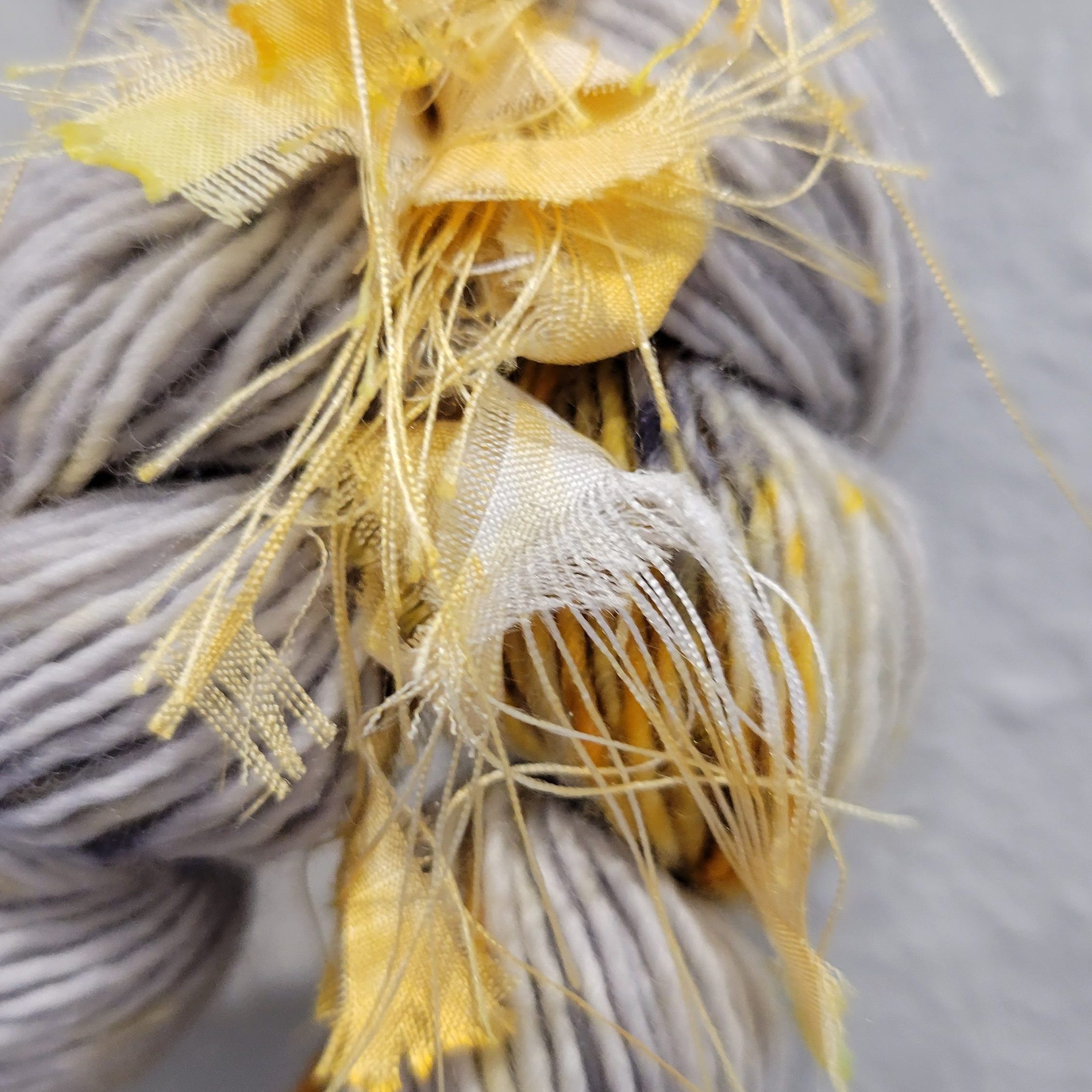 Gray plaited yarn with whispy bits of pale frayed yellow fabric emerging from the center